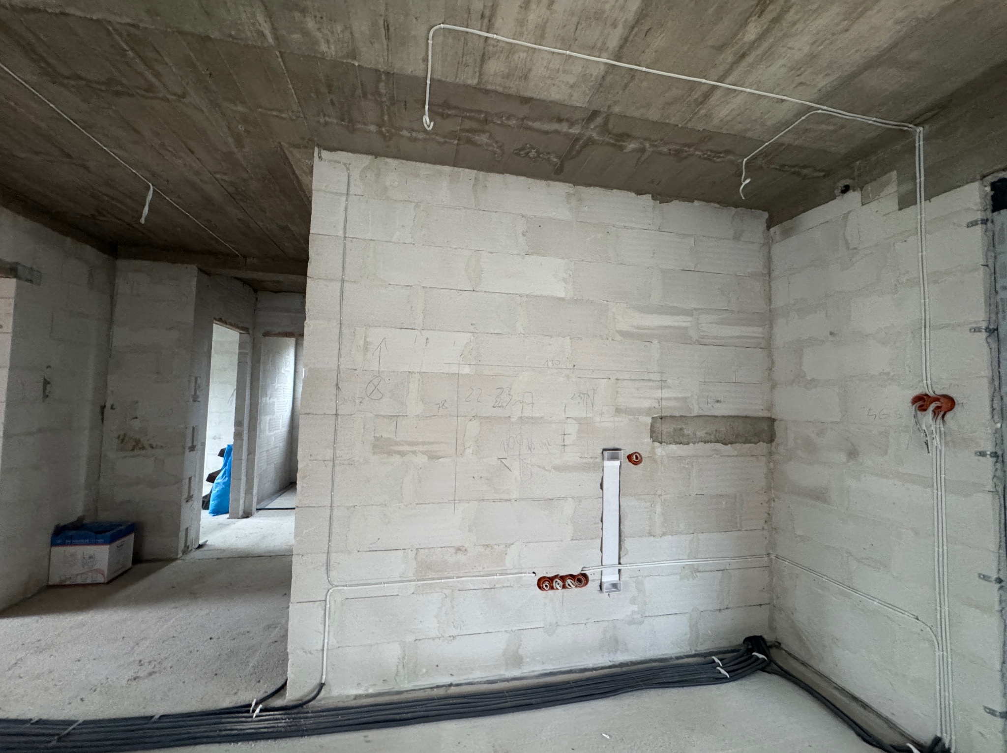 Surowy stan: ściany z betonu komórkowego z widoczną instalacją elektryczną w peszlach, kable ułożone przy podłodze. W tle widoczne kolejne pomieszczenia.