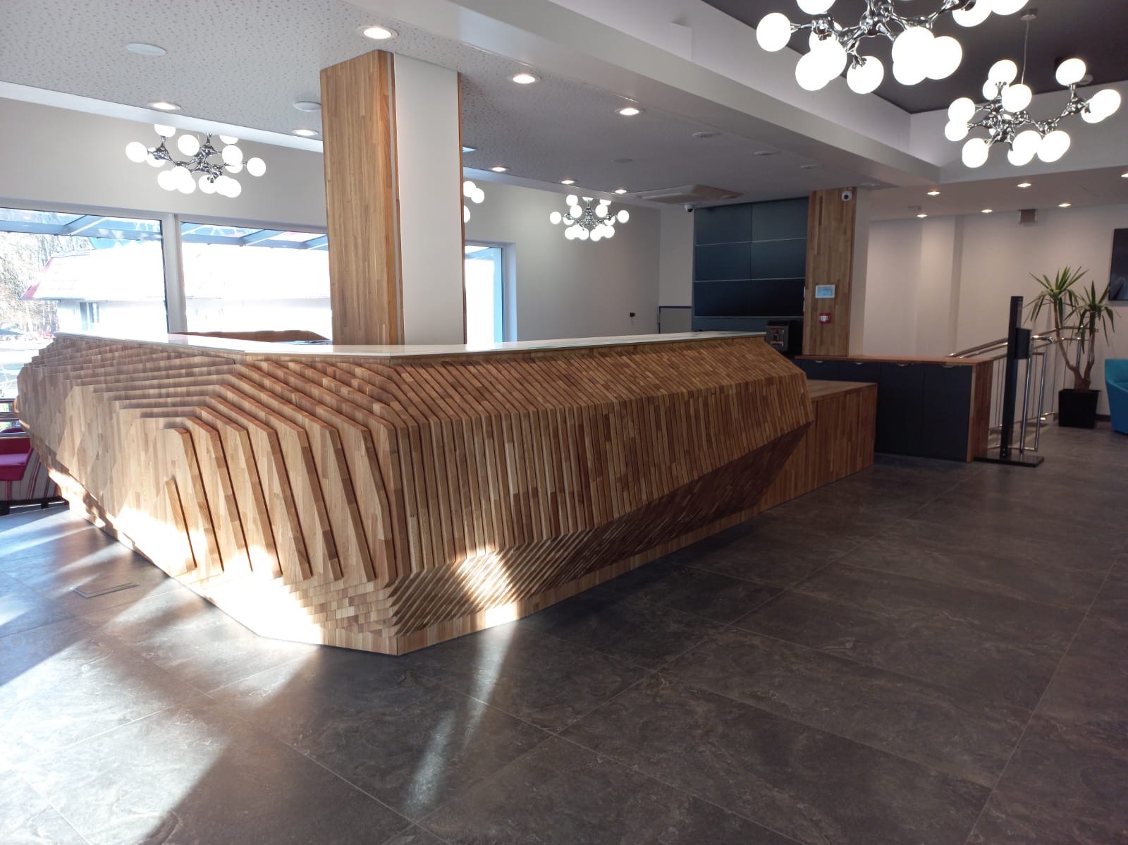 Nowoczesna recepcja z drewna w biurze, z unikalnym wzorem ułożenia desek, oświetlona lampami w stylu retro, na tle szarej podłogi z płytek.
