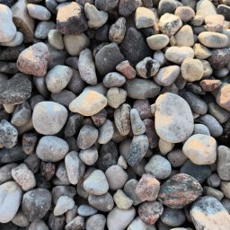 NS GARDEN STONE SPÓŁKA Z OGRANICZONĄ ODPOWIEDZIALNOŚCIĄ - Gładkie, różnokolorowe kamienie rzeczne w zbliżeniu, oświetlone z góry, tworzące naturalną mozaikę tekstur i odcieni szarości, beżu i różu. Idealne do dekoracji ogrodu.