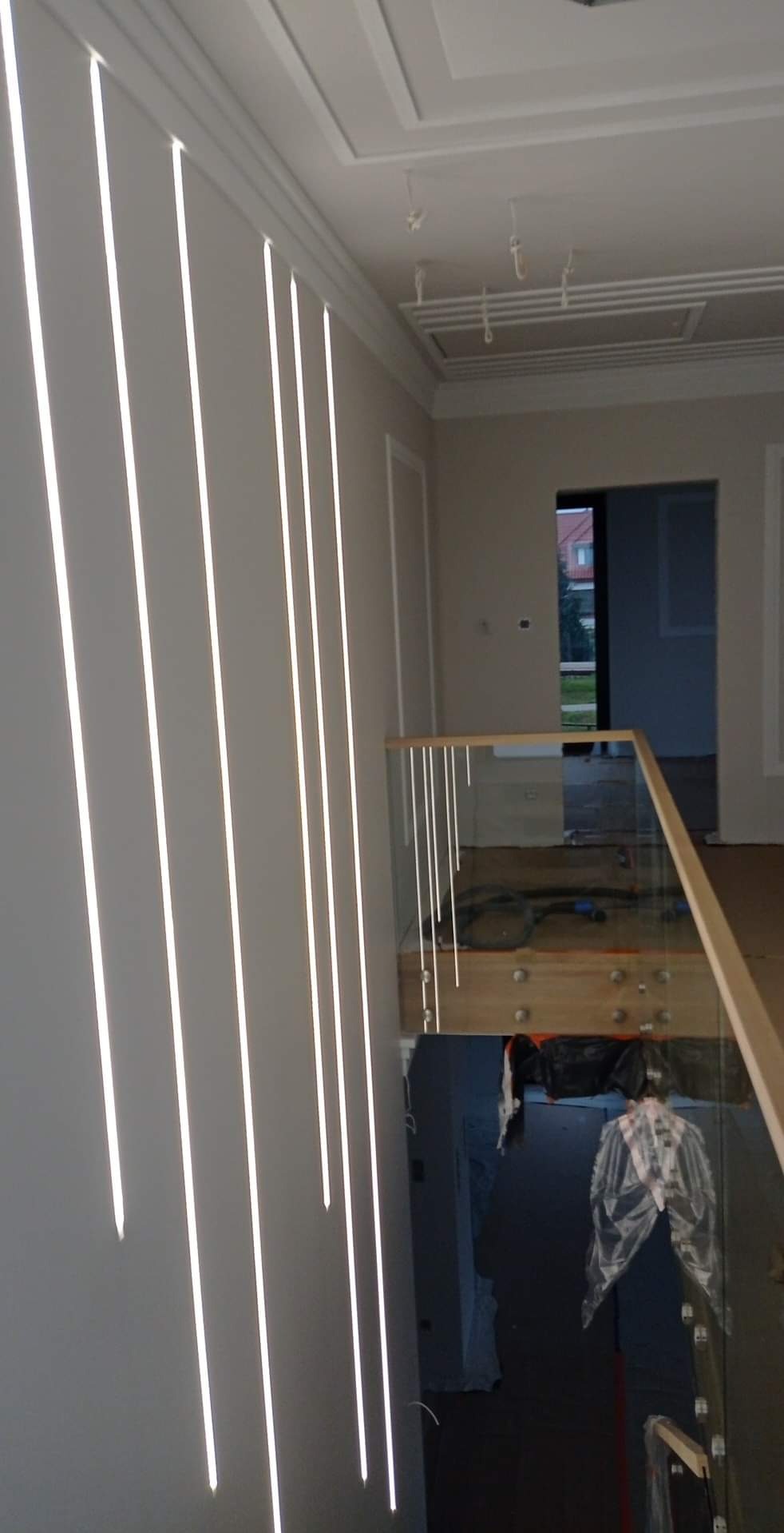 Nowoczesne oświetlenie pionowe wzdłuż ściany klatki schodowej z szklaną balustradą i drewnianymi elementami wykończeniowymi. Widok na wnętrze domu.