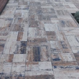 Mycie Ciśnieniowe Piotr Zieliński - Ułożona kostka brukowa w odcieniach brązu, bieli i szarości na tarasie, z widokiem na trawnik i meble ogrodowe w tle. Widoczne detale faktury kostki.