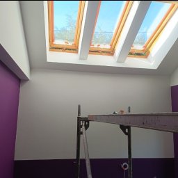M-PRO Michał Prokop usługi ogólnobudowlane - Pomieszczenie po malowaniu ścian na fioletowo i biało, widoczne okna dachowe i rusztowanie malarskie. Świeżo pomalowane ściany w dwóch odcieniach fioletu.
