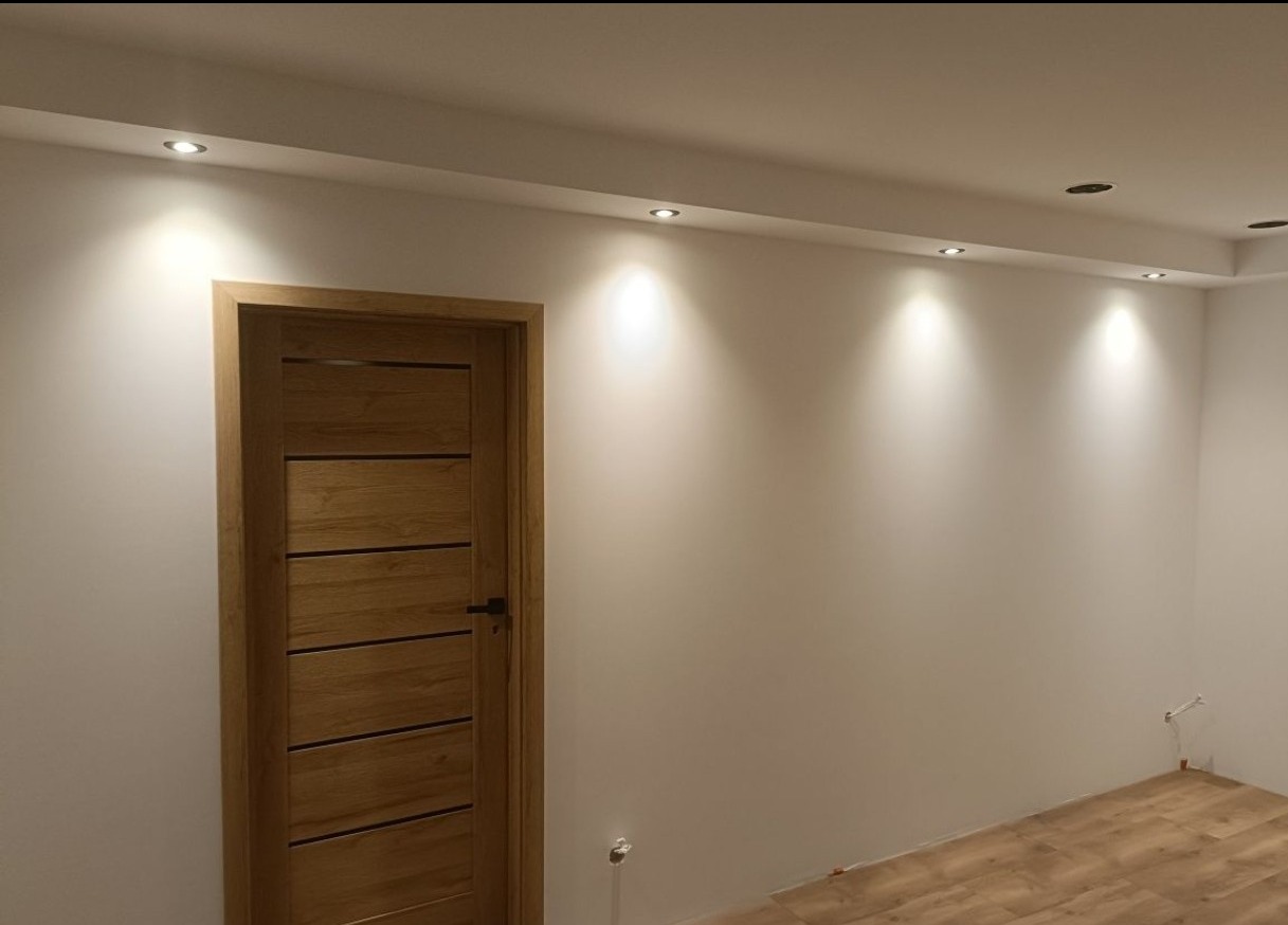 Nowoczesne wnętrze z drewnianymi drzwiami z poziomymi wstawkami i oświetleniem punktowym w suficie, świeżo po remoncie. Minimalistyczny design.