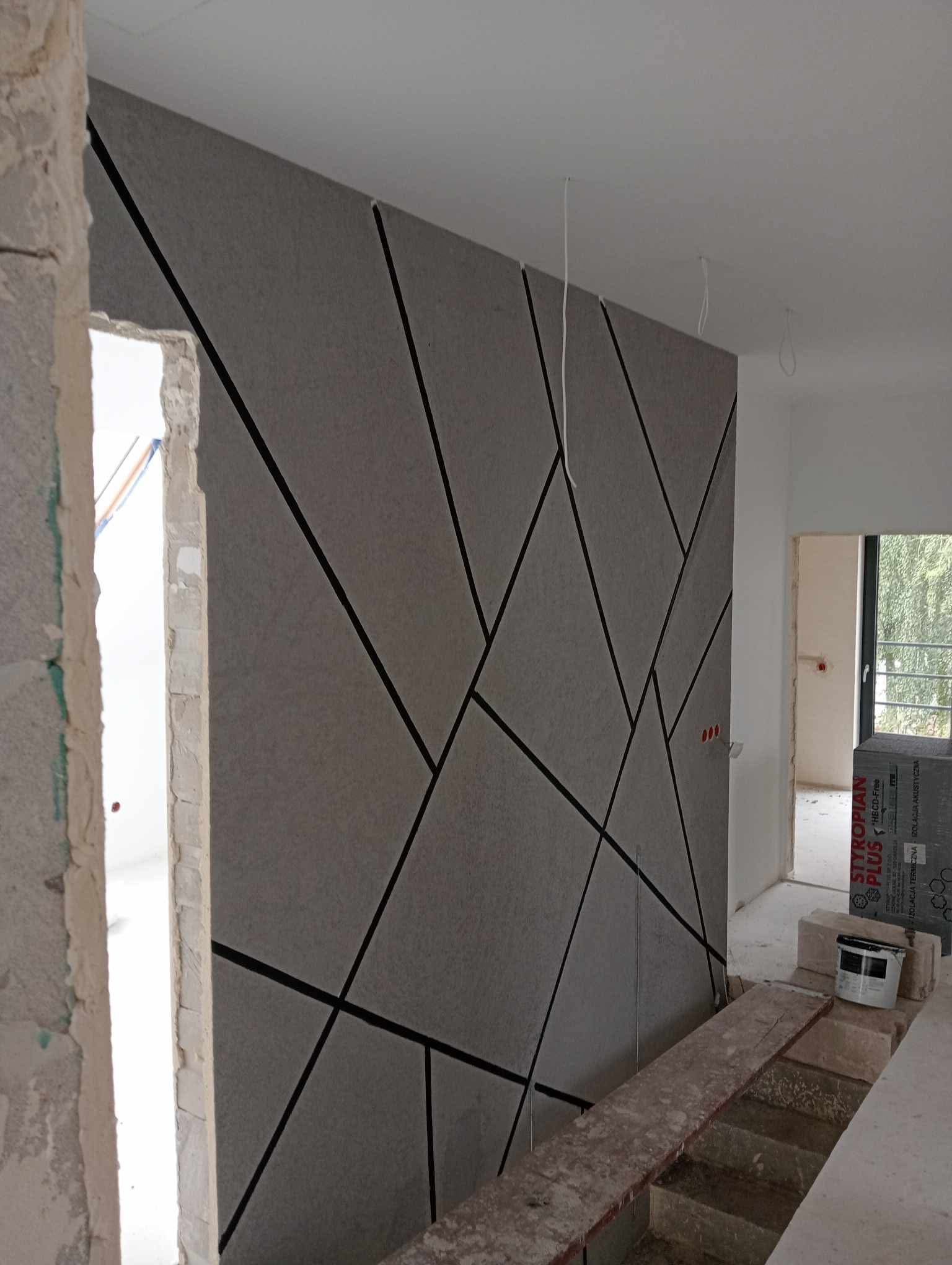 Ściana z panelami akustycznymi w geometryczny wzór, widok z bliska na surowy otwór drzwiowy i materiały budowlane. Wnętrze w trakcie wykańczania.