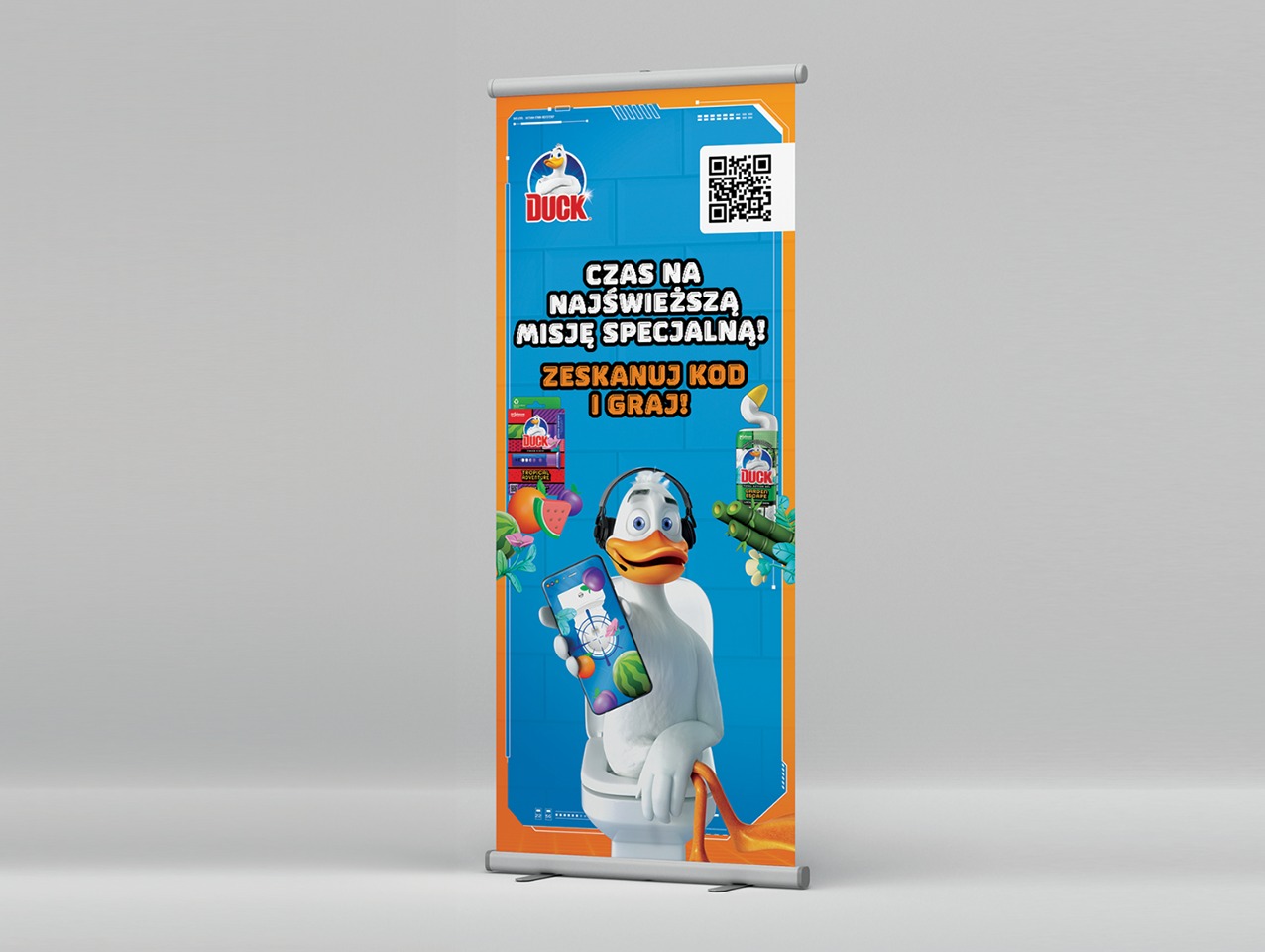 Roll-up z grafiką reklamową Duck: kreskówkowa kaczka w słuchawkach siedzi na toalecie i trzyma smartfon. Hasło: Czas na najświeższą misję specjalną! Zeskanuj kod i graj!