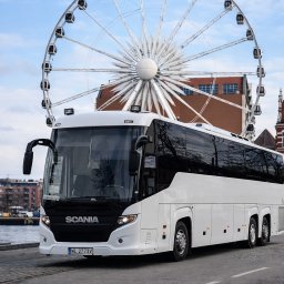 P.H.U. Tomasz Tymrakiewicz - Biały autokar Scania na tle diabelskiego młyna w Gdańsku. Nowoczesny autobus turystyczny z czarnymi szybami i elementami. Widok z przodu, tablica rejestracyjna WL 2773V.