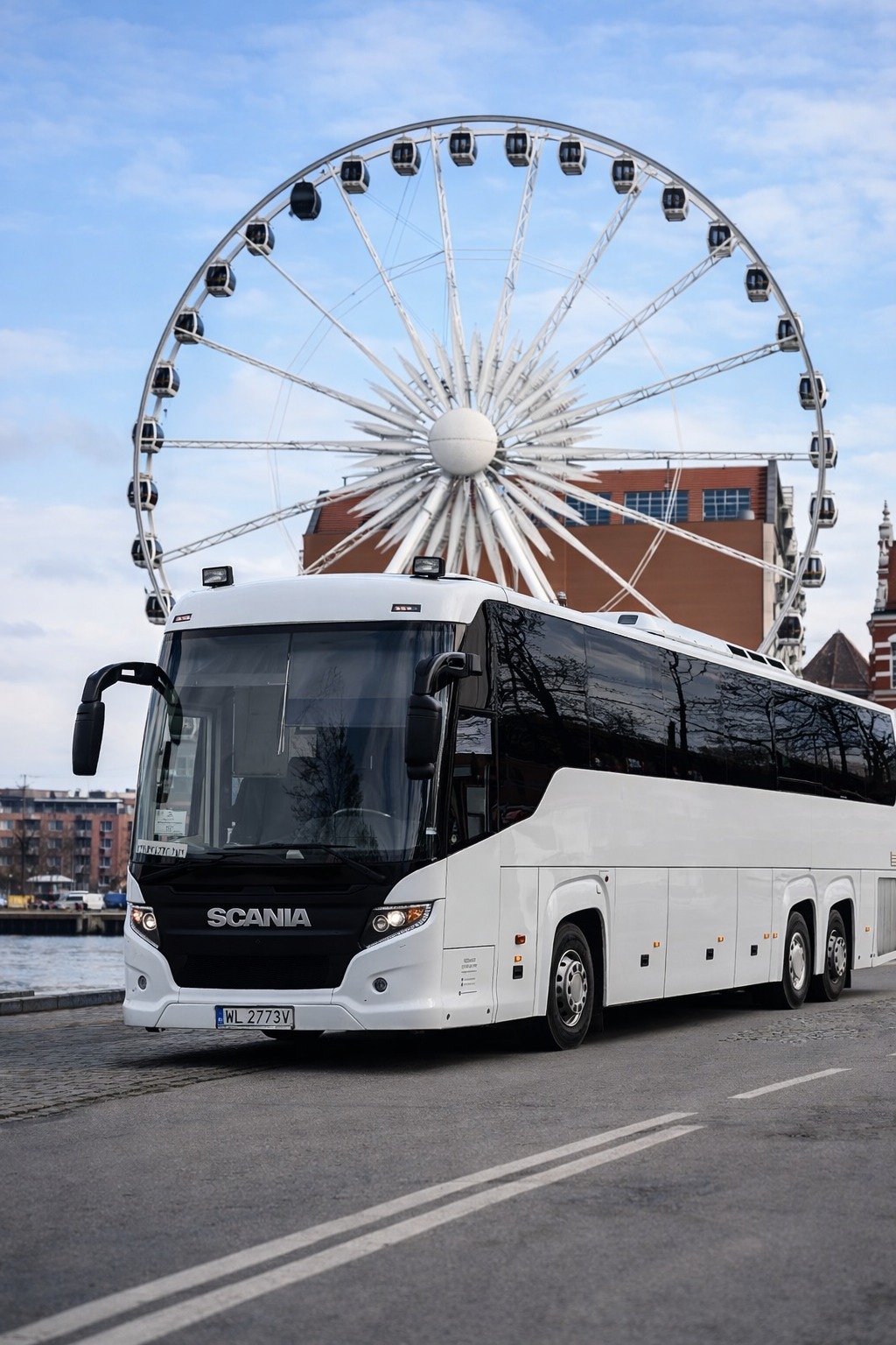 Biały autokar Scania na tle diabelskiego młyna w Gdańsku. Nowoczesny autobus turystyczny z czarnymi szybami i elementami. Widok z przodu, tablica rejestracyjna WL 2773V.
