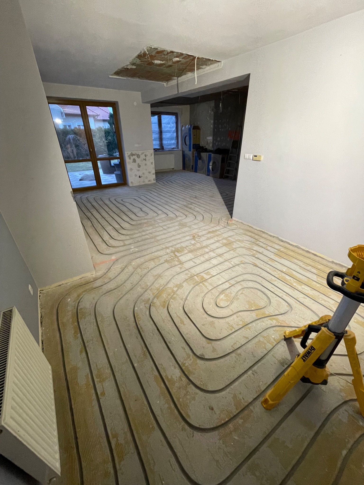 Instalacja ogrzewania podłogowego w trakcie realizacji w Rzeszowie. Widoczne ułożone rury na podłożu, przygotowane do zalania. W tle okno i fragment pomieszczenia.