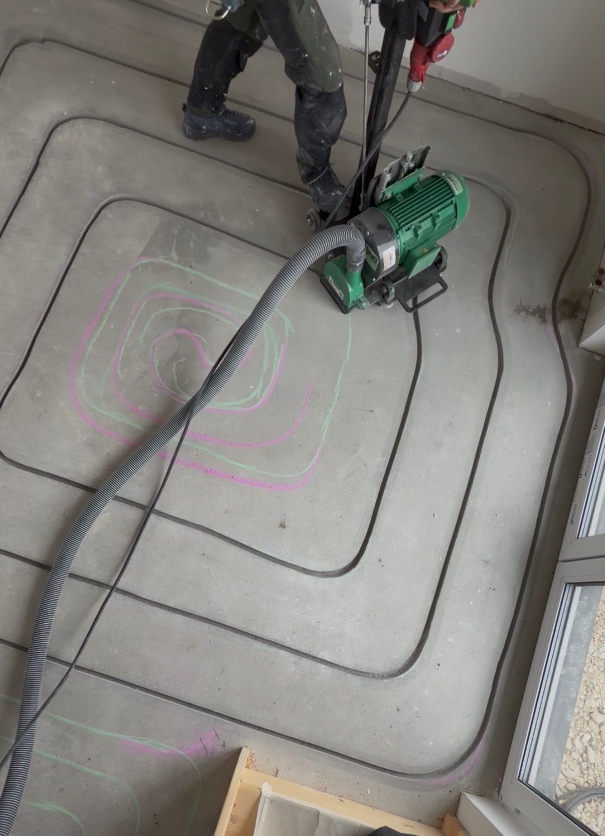 Frezowanie bruzd pod ogrzewanie podłogowe w betonie. Widoczne rury, frezarka i oznaczenia kredą. Praca w toku, z bliska, z góry.