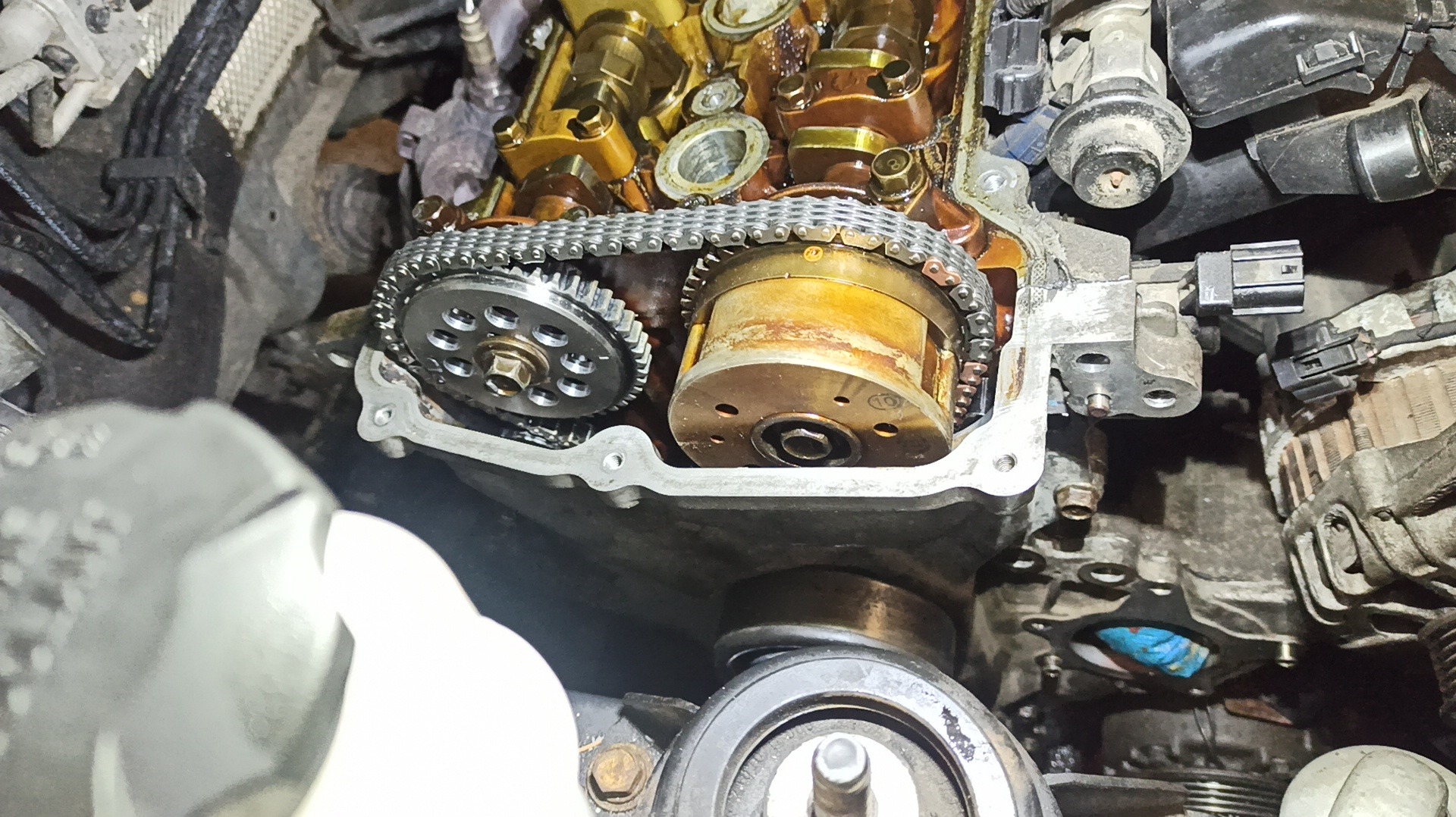 Otwarty silnik samochodowy z widocznym łańcuchem rozrządu, zębatkami i elementami głowicy. Detaliczny widok na mechanizm w trakcie naprawy lub diagnostyki.