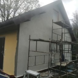 Zajdex - Elewacja domu w trakcie prac: część ściany otynkowana na szaro, druga w kolorze żółtym. Widoczne rusztowania i narzędzia malarskie. Prace wykończeniowe.