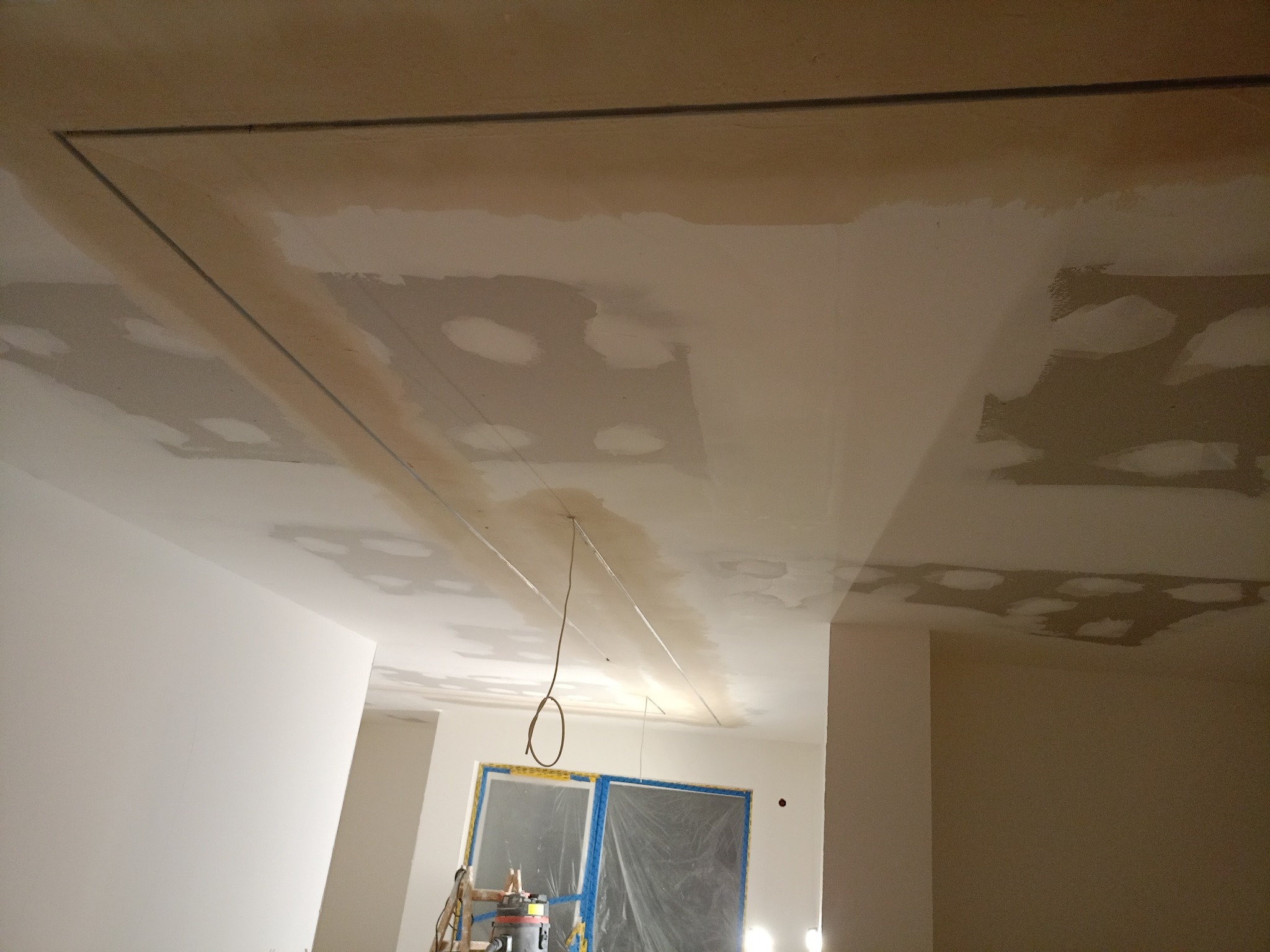 Niedokończony sufit z widocznymi śladami po łatach i szpachlowaniu, przygotowany do dalszych prac wykończeniowych. Widoczne kable i okno zabezpieczone folią.