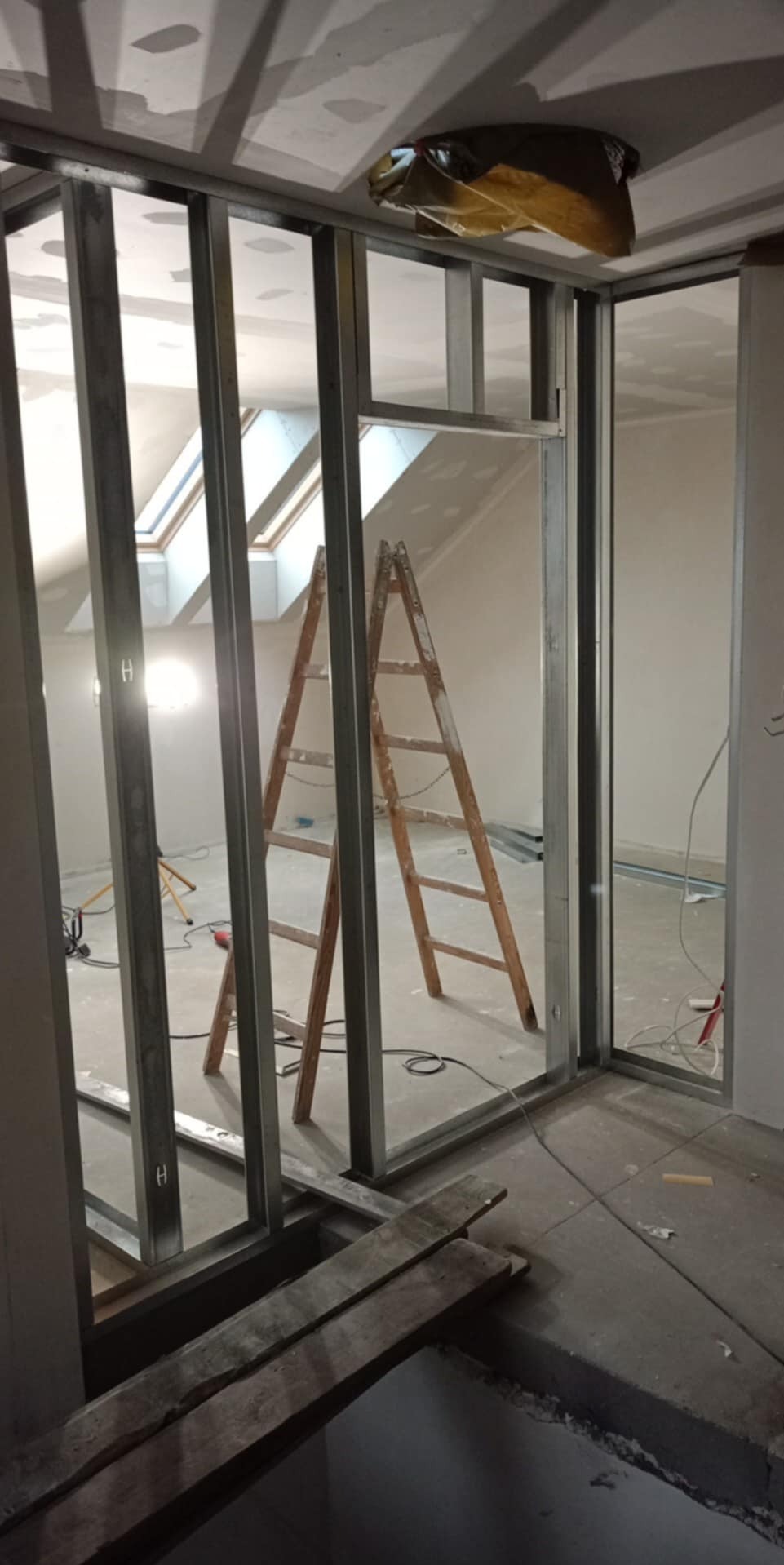 Stelaż z profili metalowych pod płytę karton-gips w surowym wnętrzu poddasza z oknami dachowymi. Widoczna drabina i narzędzia.