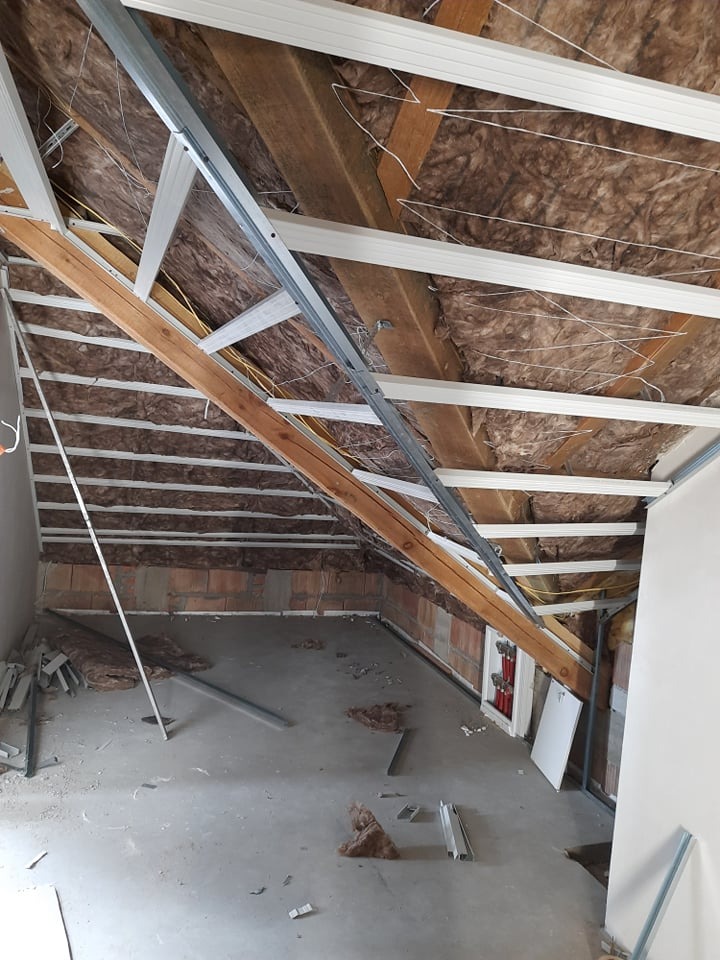 Poddasze w trakcie adaptacji: izolacja wełną mineralną, konstrukcja metalowa pod płyty gipsowe, fragment ściany z cegły. Widok na surowy stan przed wykończeniem.