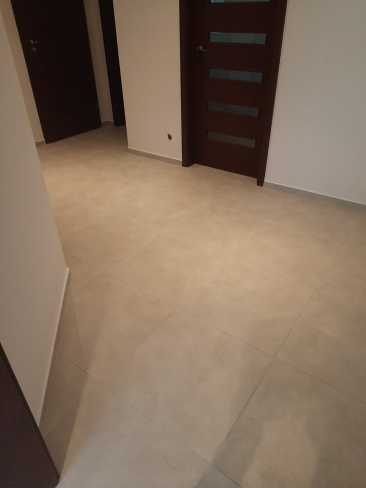 Jasne, kwadratowe płytki podłogowe w pustym pokoju z dwiema ciemnymi, drewnianymi drzwiami. Jedne z przeszkleniami. Minimalistyczny design wnętrza.