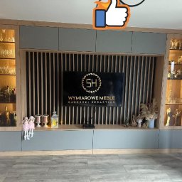 WYMIAROWE MEBLE SEBASTIAN HABERSKI - Szara zabudowa meblowa z podświetlanymi witrynami i lamelami za telewizorem. Dekoracje na półce. Nowoczesny design, jasne drewno, szare fronty.