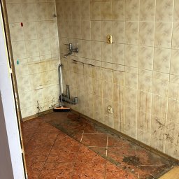 BAR-TRANS - Zdemontowana kuchnia z brudnymi, częściowo usuniętymi płytkami na ścianach i podłodze. Widoczny kran, rury i szczotka. Przygotowanie do remontu.