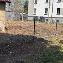 BAR-TRANS - Teren po wycince drzew i krzewów, ogrodzony siatką. Widoczne pozostałości gałęzi i pni, budynek w tle. Słoneczny dzień, wiosenna sceneria.