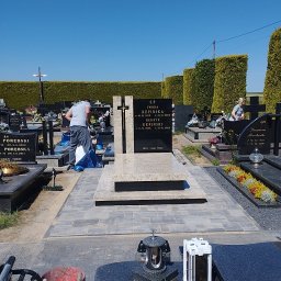 BRUKARSTWO- KAMIENIARSTWO EWA WŁÓKA - Granitowy nagrobek z krzyżem na cmentarzu, otoczony kostką brukową. Widoczna osoba sprzątająca. W tle żywopłot i inne groby. Słoneczny dzień.