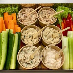 KRAKPRESS SPÓŁKA Z OGRANICZONĄ ODPOWIEDZIALNOŚCIĄ - Elegancki box cateringowy z warzywami (marchew, seler naciowy, ogórek, papryka) i dipami w papierowych miseczkach z drewnianymi łyżeczkami, idealny na przyjęcie.