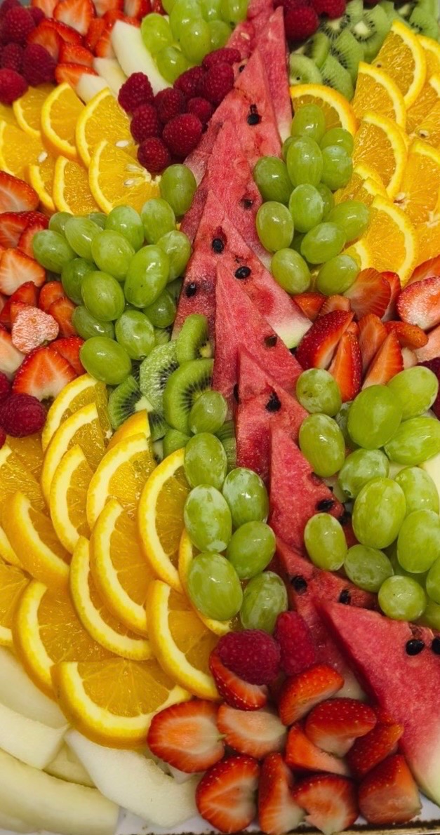 Kolorowa kompozycja owocowa: soczyste arbuzy, słodkie truskawki, orzeźwiające pomarańcze, winogrona i maliny, tworzące apetyczną mozaikę na przyjęcie.