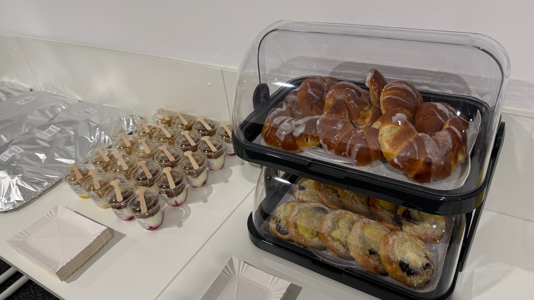 Słodki catering: rogaliki z lukrem, mini desery w kubeczkach i ciastka z owocami na białym stole, gotowe do serwowania na imprezie firmowej lub świątecznej.