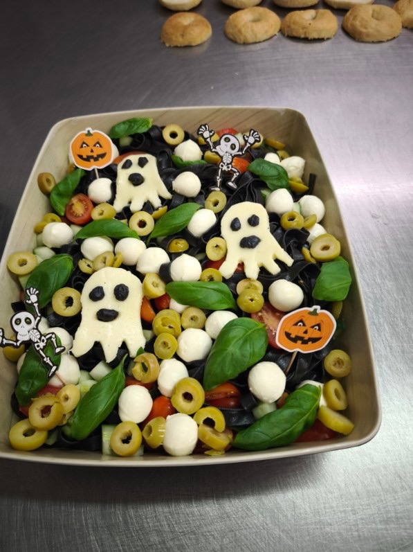 Sałatka Halloween z czarnym makaronem, mozzarellą, oliwkami, bazylią i dekoracjami: duszki z sera i dynie na patyczkach. Kreatywna propozycja cateringu tematycznego.