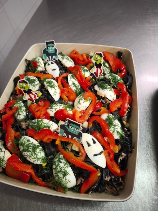 Halloweenowa sałatka z czarnym makaronem, papryką, jajkami i dekoracjami: Frankenstein, duch, zombie. Catering tematyczny w drewnianej misce.