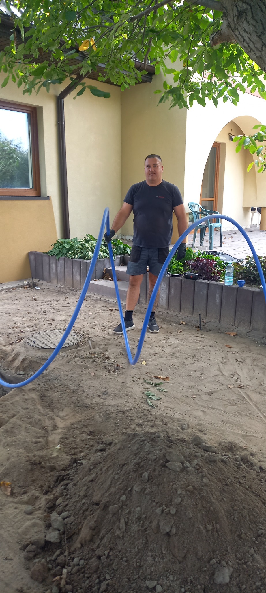 Instalator z niebieskimi rurami w Warszawie, przygotowuje się do ułożenia instalacji. Widoczne narzędzia i materiały budowlane.