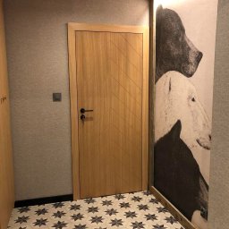 Przemek Wagner - Nowoczesne wnętrze: drewniane drzwi z wzorem w jodełkę, wzorzysta podłoga i grafika zwierząt na ścianie. Minimalistyczny design z akcentem na detale.