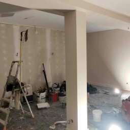 Przemek Wagner - Wnętrze w trakcie remontu: ściany po szpachlowaniu, widoczne narzędzia (szczególnie szlifierka), drabina i wiadro z farbą. Przygotowanie do malowania.