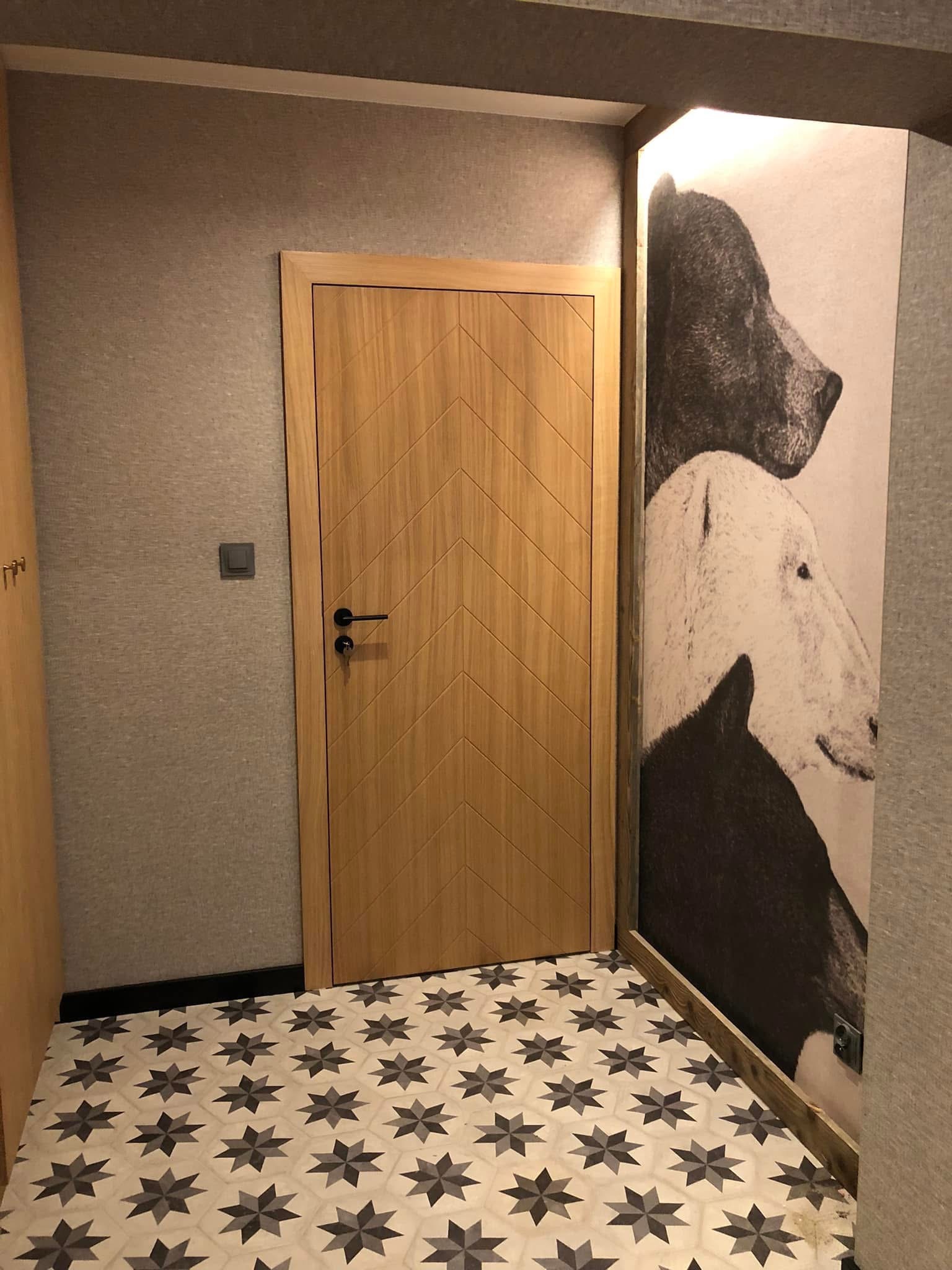 Nowoczesne wnętrze: drewniane drzwi z wzorem w jodełkę, wzorzysta podłoga i grafika zwierząt na ścianie. Minimalistyczny design z akcentem na detale.