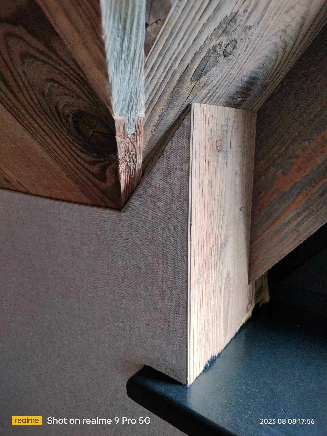 Wykończenie poddasza z drewnianymi elementami konstrukcyjnymi i szarą płytą. Widoczne detale łączeń i faktura materiałów. Ujęcie z dołu, podkreślające geometrię.