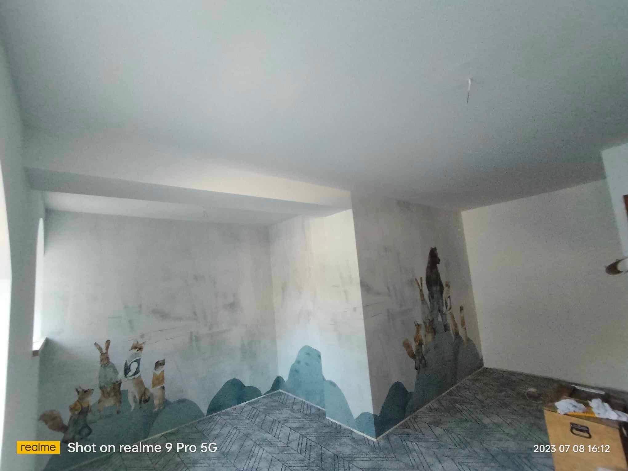 Pokój po malowaniu z motywem zwierząt w ubraniach na ścianach i wzorem gór u dołu. Nietypowa dekoracja ścian w pokoju dziecięcym. Podłoga w szarym wzorze.