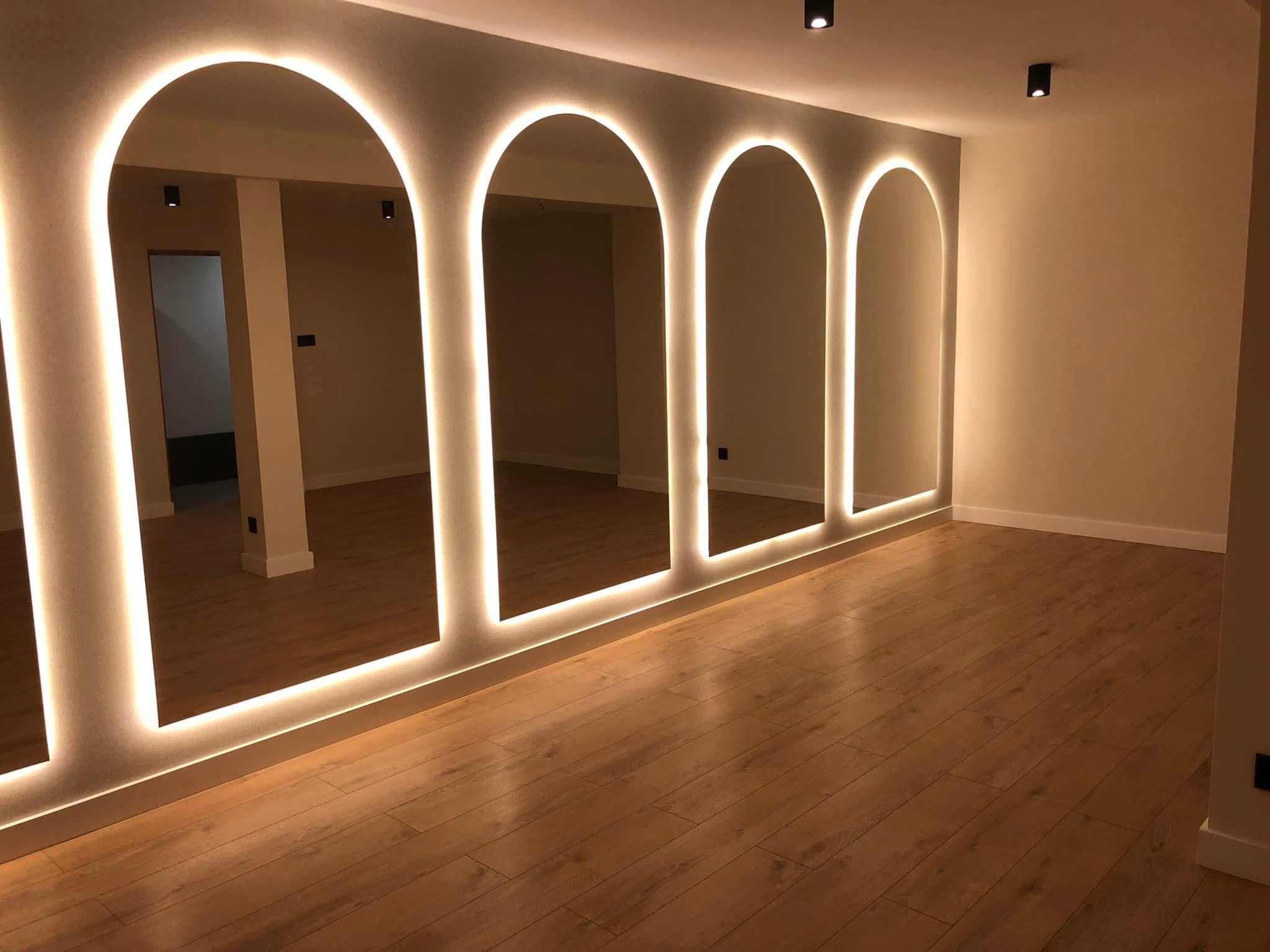 Nowoczesne lustra łukowe z podświetleniem LED w Zakopanem, odbijające parkiet. Minimalistyczny design, ciepłe światło, gładkie ściany. Idealne do salonu lub sypialni.