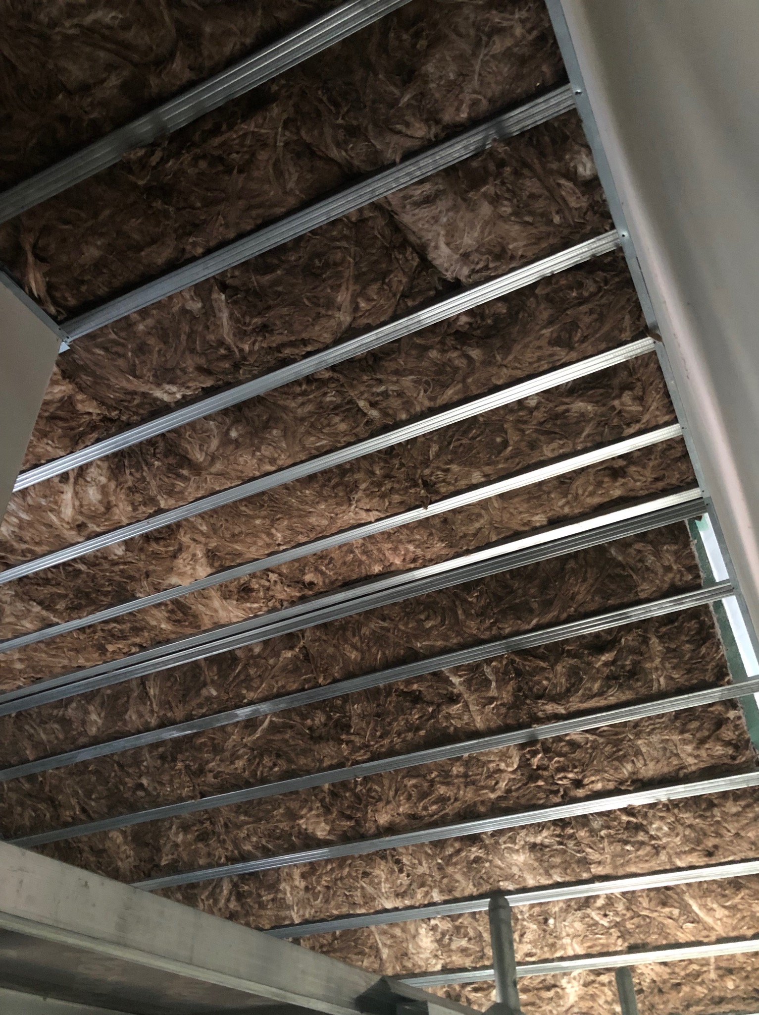 Sufit z izolacją z wełny mineralnej, widoczne metalowe profile konstrukcyjne. Ujęcie z dołu, podkreślające strukturę i detale izolacji.