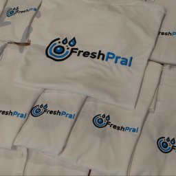 PATI-HAFT MARZENNA POŁETEK - Stos białych koszulek z identycznym, niebiesko-czarnym logo 'FreshPral' umieszczonym na piersi. Różne kroje koszulek, ułożone warstwami, tworzą kompozycję.