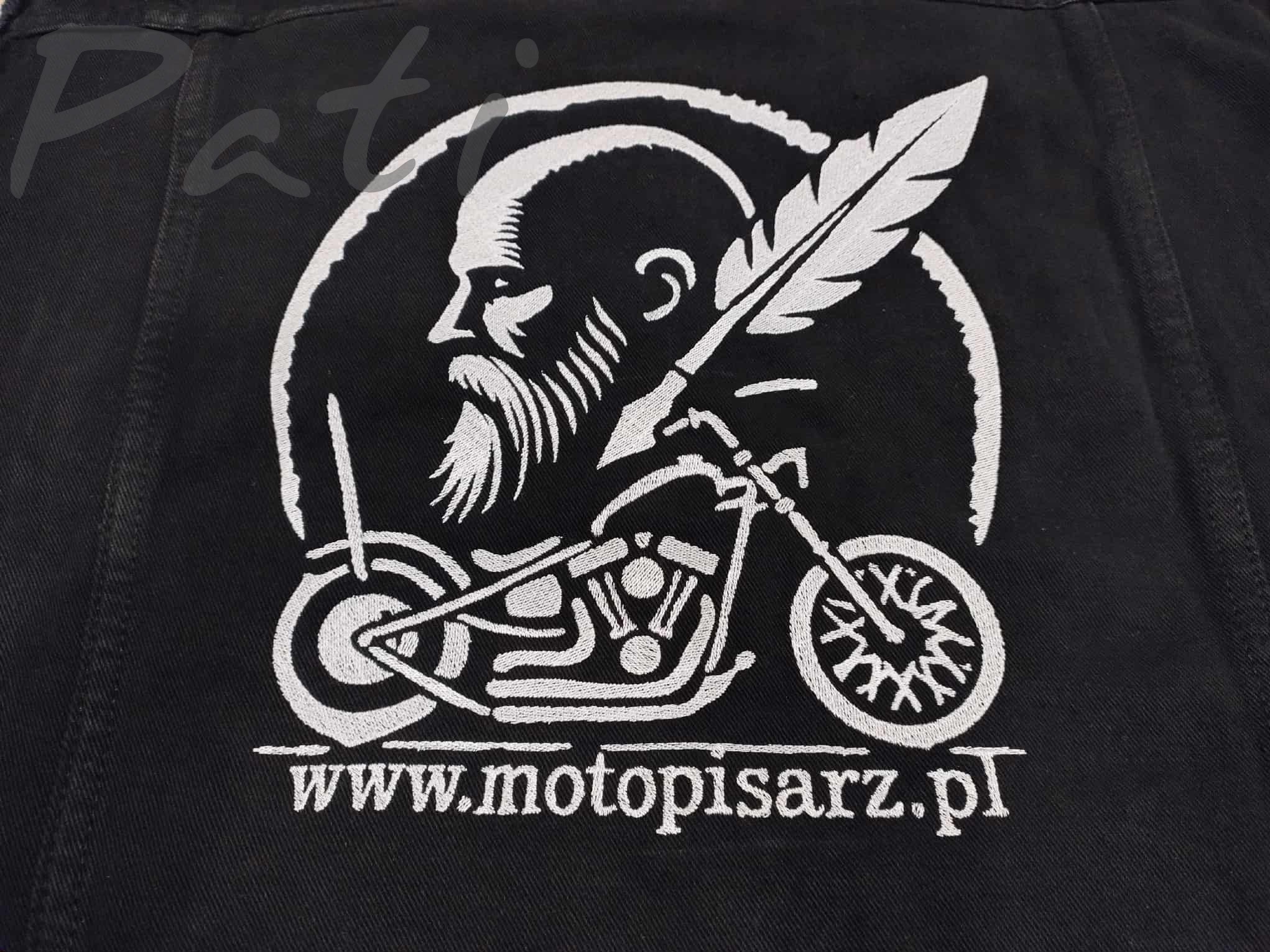 Czarna kurtka jeansowa z białym haftem: brodaty mężczyzna z piórem na motocyklu i adresem strony www.motopisarz.pl. Detal haftu, bliski kadr.