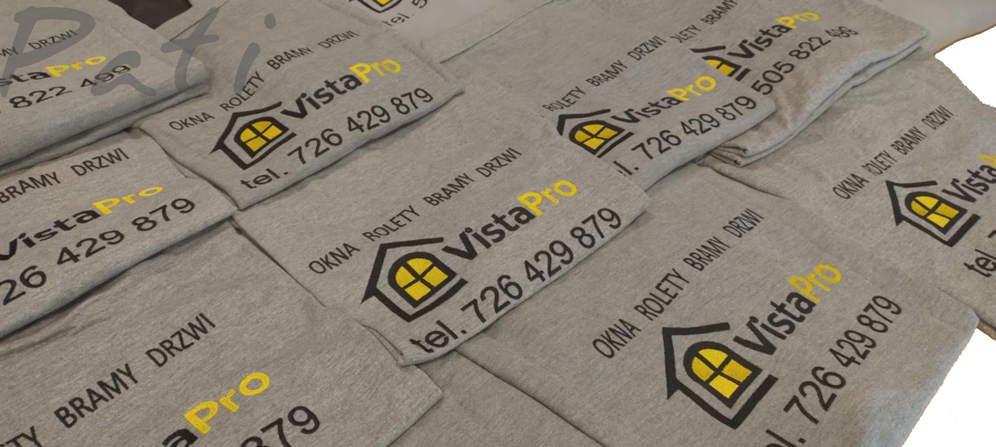 Szare koszulki z nadrukiem logo firmy VistaPro (okna, rolety, bramy, drzwi) w kolorach czarnym i żółtym, ułożone warstwami. Widoczne numery telefonów.