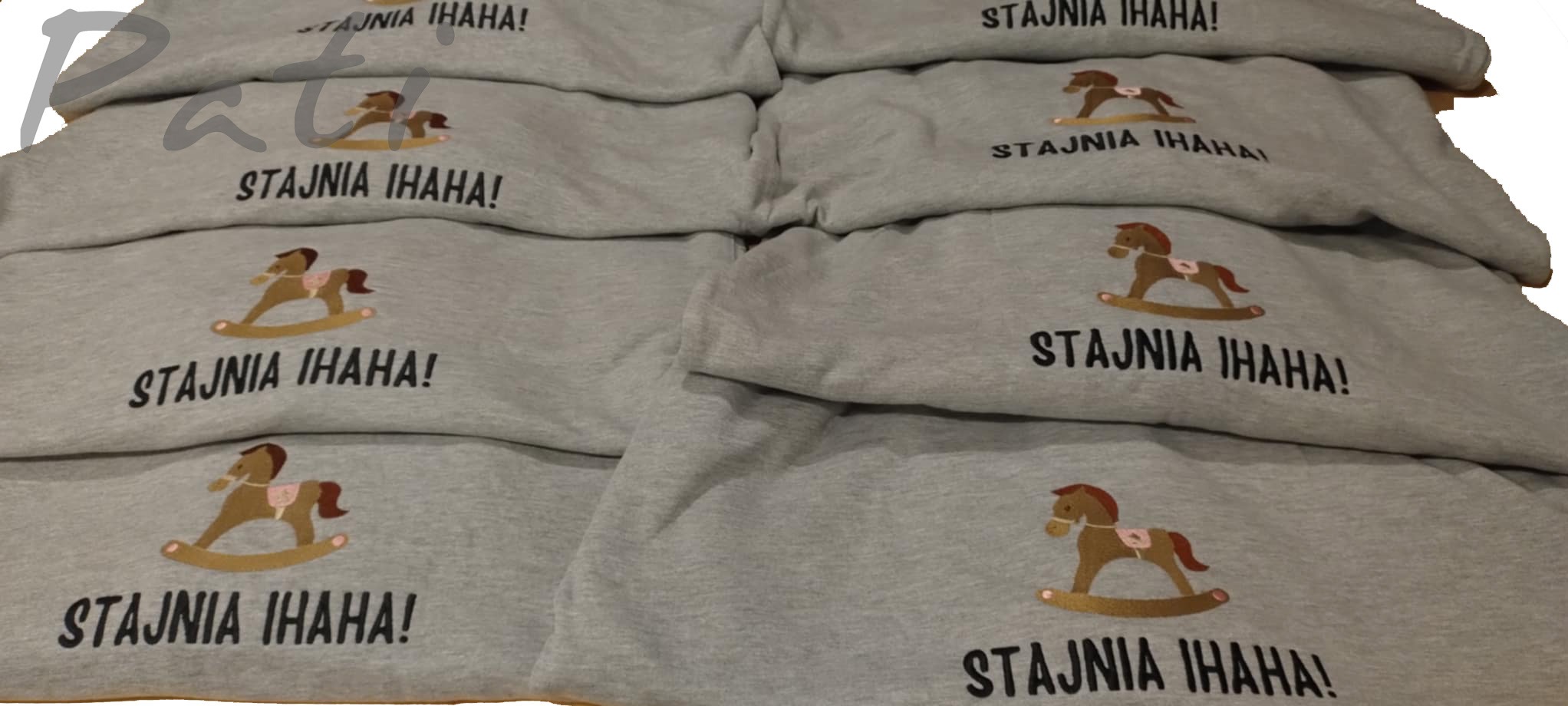 Stos szarych bluz z haftowanym motywem konika na biegunach i napisem 'Stajnia Ihaha!', ułożonych warstwami, prezentujących detale wykonania.