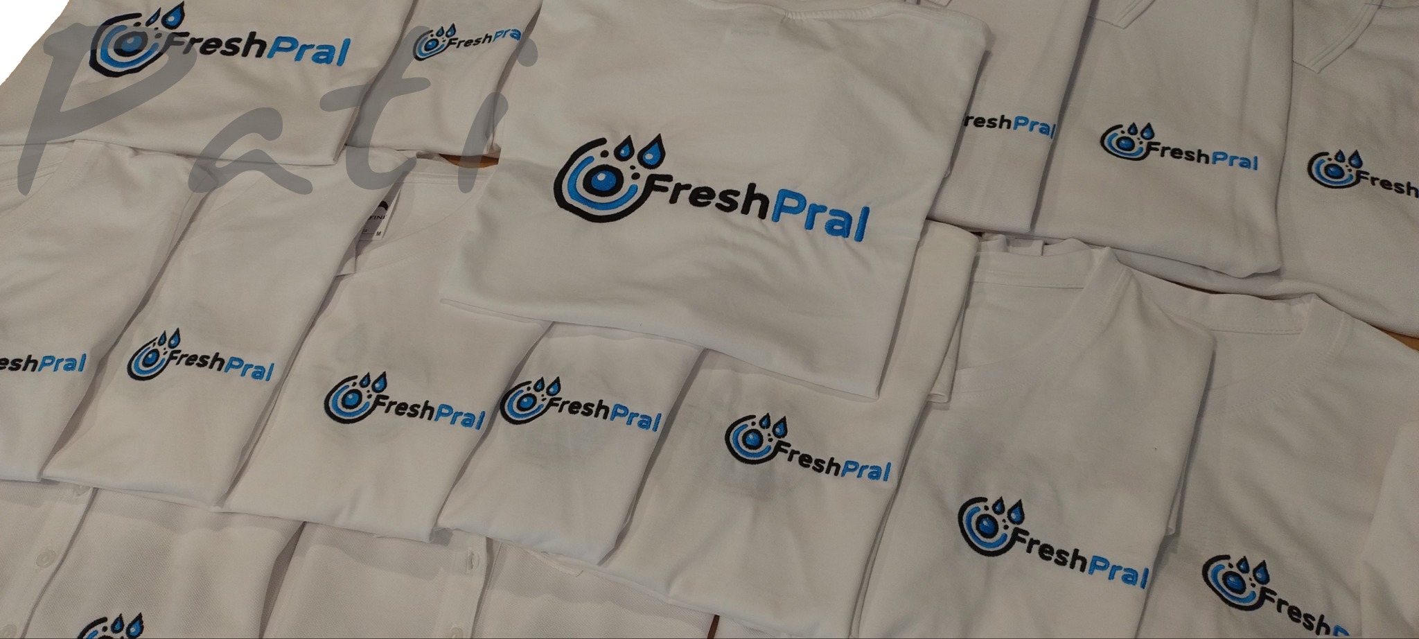 Stos białych koszulek z identycznym, niebiesko-czarnym logo 'FreshPral' umieszczonym na piersi. Różne kroje koszulek, ułożone warstwami, tworzą kompozycję.