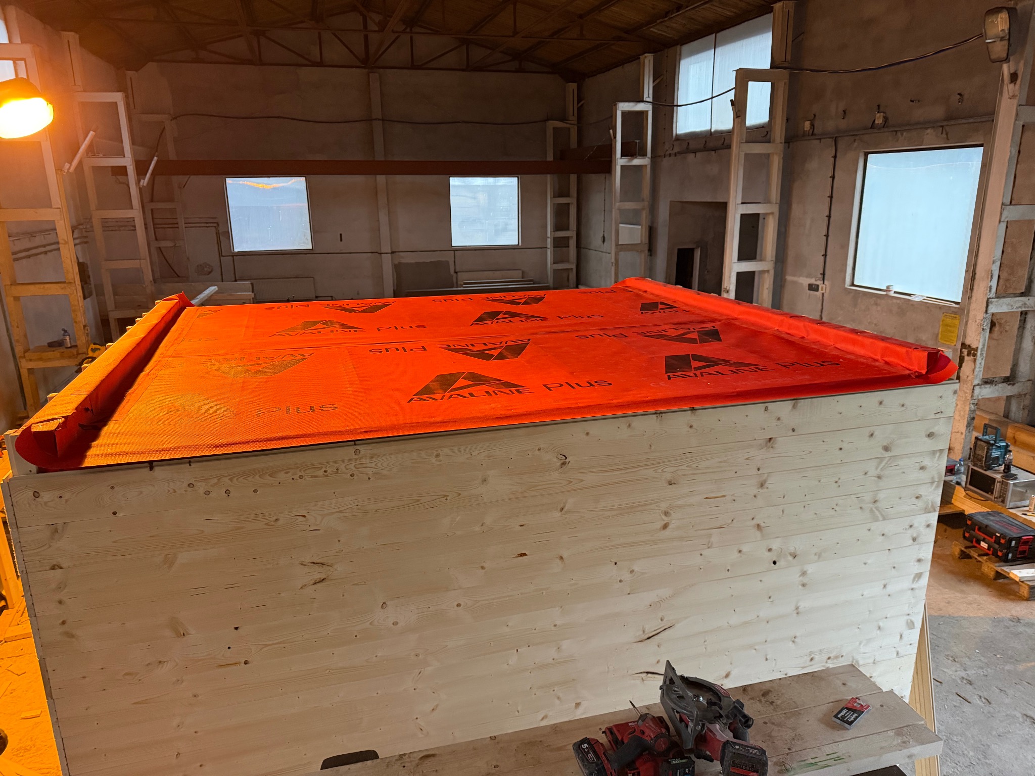 Konstrukcja domu w Zgorzelcu, drewniane ściany z membraną Avaline Plus, narzędzia na stole. W tle surowy budynek w trakcie prac wykończeniowych.