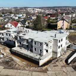 Przedsiębiorstwo Budowlane Damian Kleinszmidt - Wysoki kąt na budowę dwupiętrowego budynku z żelbetu w stanie surowym otwartym, z dźwigiem i pracownikami na dachu, na tle zabudowy miejskiej.