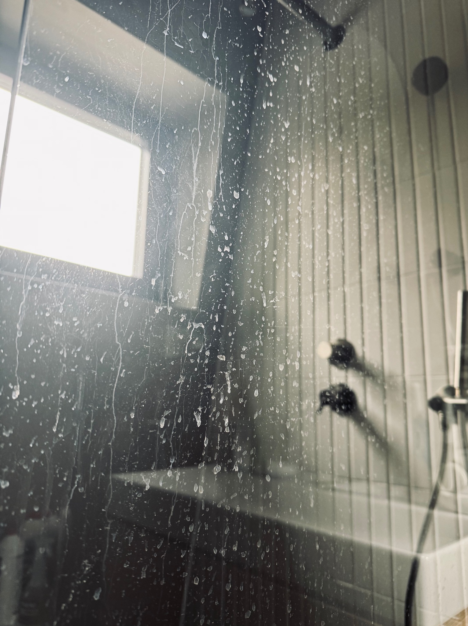 Zabrudzona kabina prysznicowa z widocznymi zaciekami i osadem, na tle białych płytek i okna. Widoczne elementy armatury.