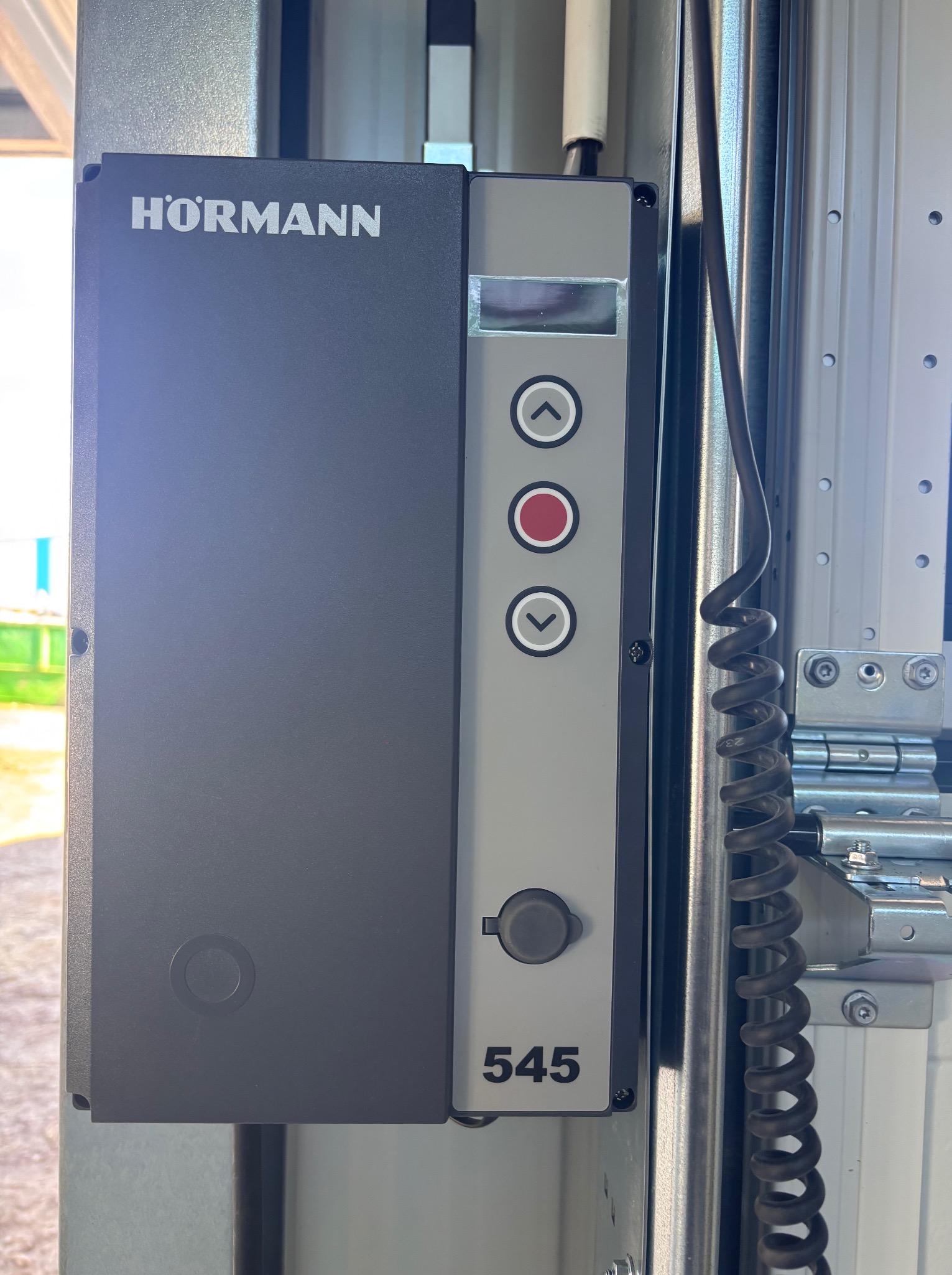 Panel sterowania bramy garażowej Hörmann 545 z przyciskami góra/dół i stop, zamontowany na szynie. Widoczne elementy konstrukcyjne bramy.
