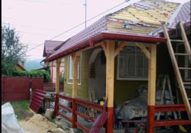 Dom w trakcie wymiany pokrycia dachowego z czerwoną rynną, widoczna drabina i materiały budowlane. Częściowo odsłonięta konstrukcja dachu.