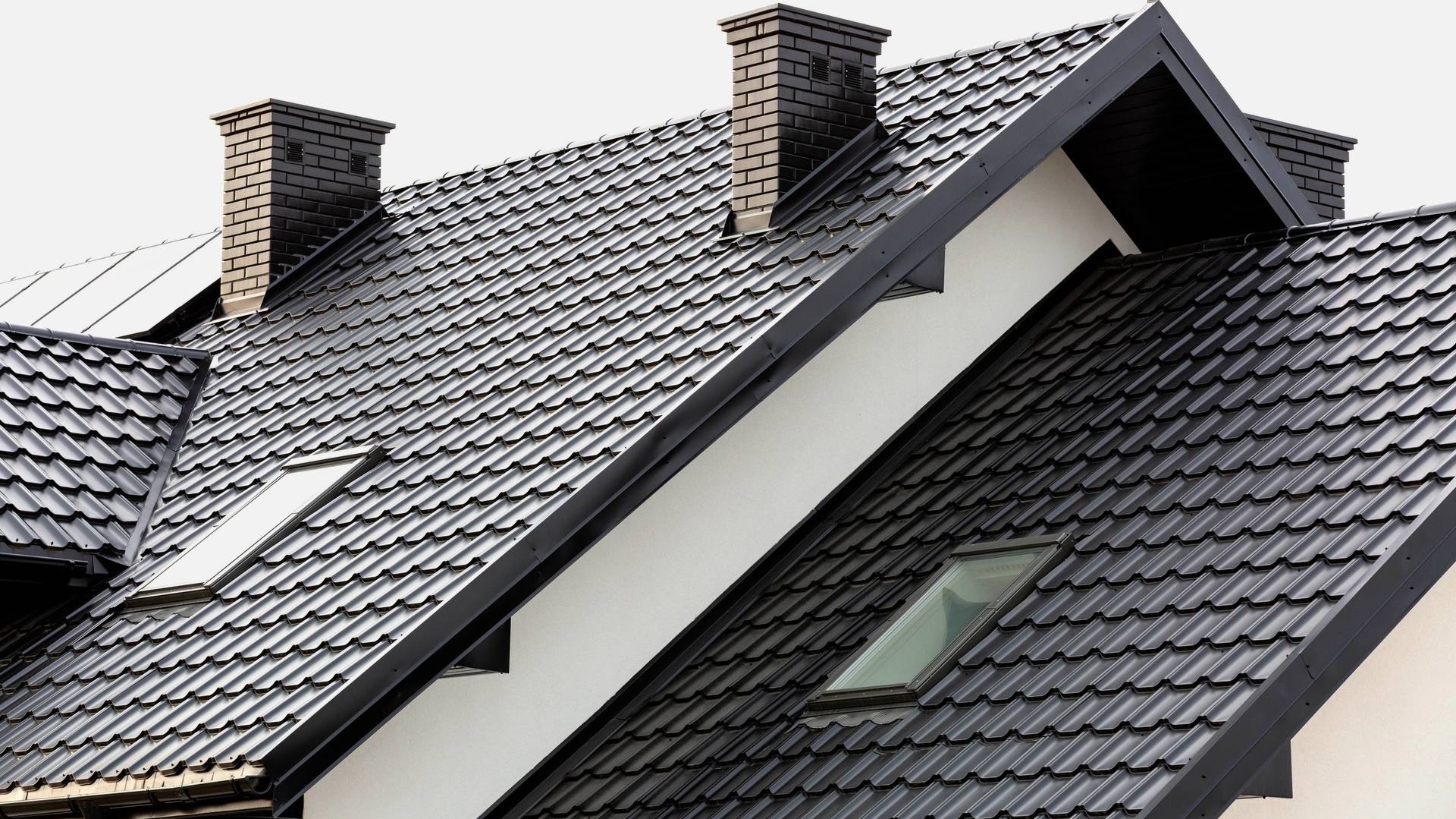 Czarny dach z dachówką ceramiczną, dwa kominy z cegły i okna dachowe. Nowoczesne wykończenie, białe ściany. Ujęcie z dołu, podkreślające geometrię dachu.