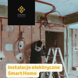 STALIMPORT SPÓŁKA Z OGRANICZONĄ ODPOWIEDZIALNOŚCIĄ - Elektryk w trakcie pracy nad instalacją elektryczną w surowym wnętrzu. Widoczne przewody, puszki i drabina. Ceglana ściana z wywierconymi otworami.