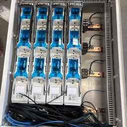 CONVION SPÓŁKA Z OGRANICZONĄ ODPOWIEDZIALNOŚCIĄ - Rozdzielnica elektryczna z modułami Wöhner, widok z góry. Widoczne przewody, szyny miedziane i elementy zabezpieczające. Biała obudowa z szarym tłem.