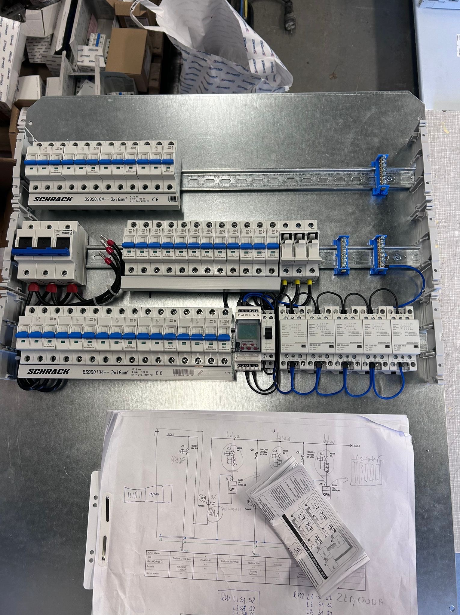Rozdzielnica elektryczna Schrack z zabezpieczeniami, przewodami i schematem. Widoczne bezpieczniki, wyłączniki, listwy zaciskowe i dokumentacja techniczną.